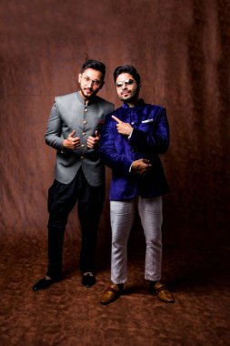 İki Hintli erkek etnik ya da geleneksel kıyafetler giyer, Sherwani ya da Kurta pijamalı erkek modeller, kahverengi grunge arka planında durup poz verirler, seçici bir odak noktası vardır.