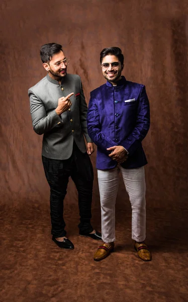 two Indian men wears ethnic or traditional cloths,  Male fashion models with sherwani or Kurta Pyjama, standing and posing over brown grunge background, selective focus
