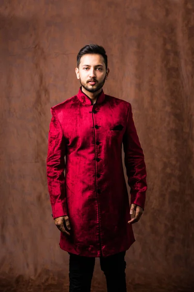 Indian man in traditional wear OR kurta / pyjama cloths.  Male fashion model in sherwani, posing / standing against brown grunge background, selective focus