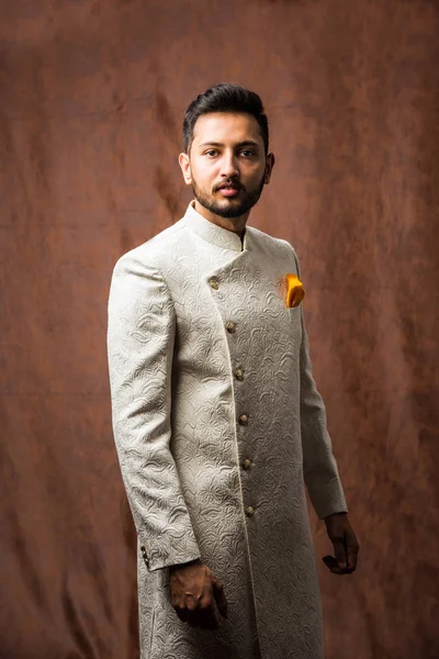 Indian man in traditional wear OR kurta / pyjama cloths.  Male fashion model in sherwani, posing / standing against brown grunge background, selective focus
