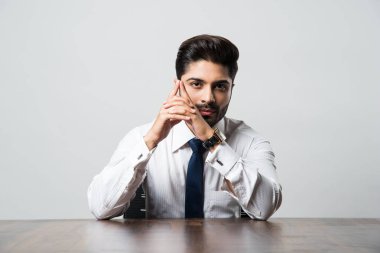 Gri arkaplanda masa / masada oturan Hintli erkek işadamının portresi.