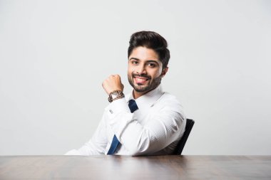 Gri arkaplanda masa / masada oturan Hintli erkek işadamının portresi.