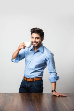 İş yerinde kahve / çay içen Hintli işadamı, masada ya da elinde fincan ve fincan tabağıyla oturuyor. 