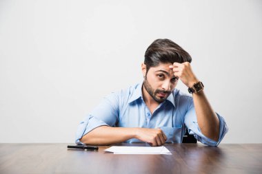 Stresli Hintli iş adamı ofis masasında çalışırken baş ağrısı ya da migren ağrısı çekiyor