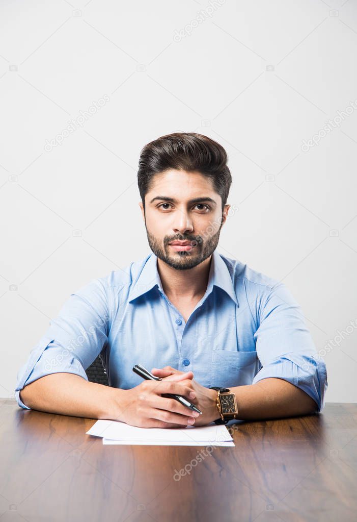 Indian businessman writing a document while sitting at desk or work station