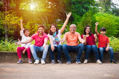 Hint ailesi pikniğin tadını çıkarıyor - Asyalı bir ailenin çok nesli parktaki küçük bir duvarın yanında ya da yanında oturuyorlar. seçici odak