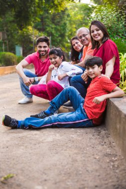 Hint ailesi pikniğin tadını çıkarıyor - Asyalı bir ailenin çok nesli parktaki küçük bir duvarın yanında ya da yanında oturuyorlar. seçici odak