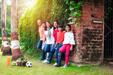 Hintli aile sürüngenlerle kaplı duvarın önünde kuyrukta bekliyor. Parkta ya da bahçede yaşayan Asyalı bir ailenin çok nesli eğlenceli ve sağlıklı bir aile hayatı yaşıyor.