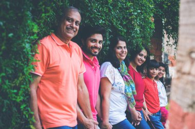 Hintli aile sürüngenlerle kaplı duvarın önünde kuyrukta bekliyor. Parkta ya da bahçede yaşayan Asyalı bir ailenin çok nesli eğlenceli ve sağlıklı bir aile hayatı yaşıyor.