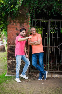 Hintli / Asyalı kıdemli baba oğlu, kırmızı tuğla duvara karşı kot ve tişört giyerken fotoğraf için poz veriyor.
