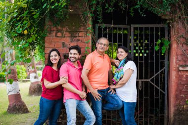 Dört kişilik Hint ailesi parkta ya da bahçede tuğla duvara karşı duruyor ve eğlenceli, sağlıklı bir aile hayatı yaşıyorlar.