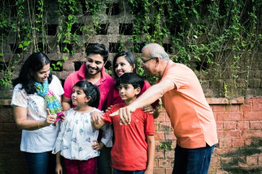 Hintli aile sürüngenlerle kaplı duvarın önünde kuyrukta bekliyor. Parkta ya da bahçede yaşayan Asyalı bir ailenin çok nesli eğlenceli ve sağlıklı bir aile hayatı yaşıyor.