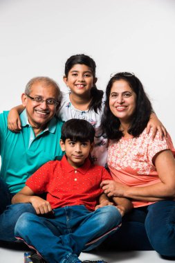 Beyaz arka planda otururken büyükannesi ve büyükbabası gülümseyen Hintli çocuklar, seçici bir odak.