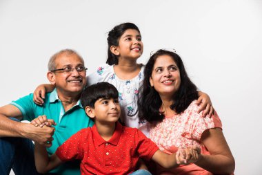 Beyaz arka planda otururken büyükannesi ve büyükbabası gülümseyen Hintli çocuklar, seçici bir odak.