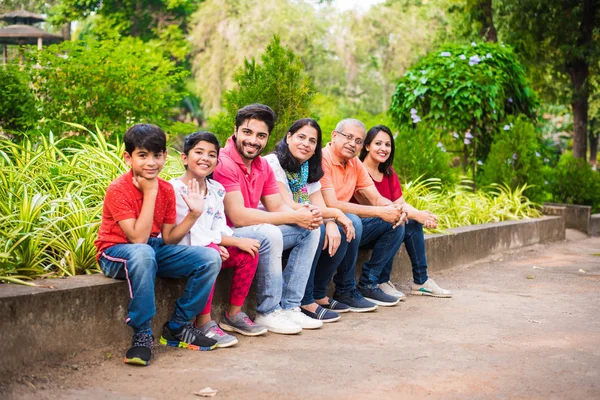 Indian Family enjoying Picnic - Multi generation of asian family sitting over or near small wall in park, outdoor. selective focus