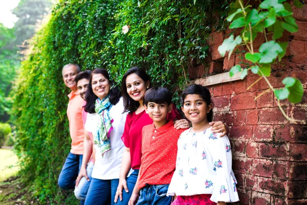 Indian family standing in line against wall covered with creepers. Multi generation of asian family in park or garden having fun, healthy family life concept