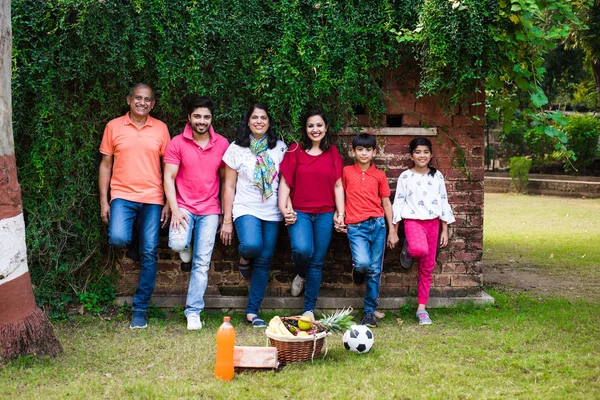 Indian family standing in line against wall covered with creepers. Multi generation of asian family in park or garden having fun, healthy family life concept