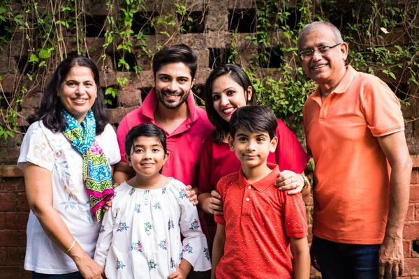 Indian family standing in line against wall covered with creepers. Multi generation of asian family in park or garden having fun, healthy family life concept
