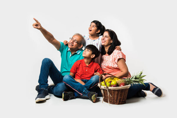 Индийские дети с бабушкой и дедушкой улыбаются, сидя на белом фоне в помещении, избирательный фокус
