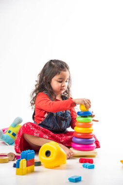 Beyaz arka planda renkli blok oyuncaklarıyla oynayan şirin küçük Hintli / Asyalı kız