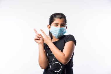 Hintli Kız Çocuk Kirliliğe karşı güvenlik önlemi olarak Sağlık Yüzü Maskesi Giyiyor veya Virüs Yayılıyor, beyaz arka plana karşı izole olarak ayakta duruyor