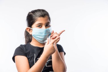 Hintli Kız Çocuk Kirliliğe karşı güvenlik önlemi olarak Sağlık Yüzü Maskesi Giyiyor veya Virüs Yayılıyor, beyaz arka plana karşı izole olarak ayakta duruyor