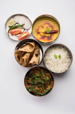 Indian vegetarian Lunch Box or Tiffin made up of stainless steel for office or workplace, includes Dal Fry, Bhindi Masala, Rice with chapati and salad clipart