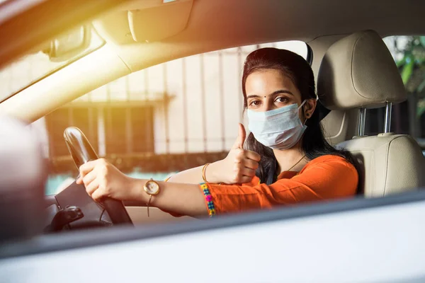 Beautiful Indian young girl in a mask sitting in a car, protective mask against coronavirus, driver on a city street during covid-19 pandemic