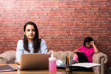 Çalışan Hintli anne, çocuk salgınında evde çalışıyor. Dizüstü bilgisayar kullanan bir kadın ve sevimli çocuk. Rahat evdeki Freelancer işyeri. Mutlu anne ve kız.