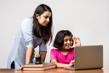 Coronavirus salgını ve eğitim konsepti - kilitlenme ve okul kapanması. Hint Anne, kızının evde online ders çalışmasına yardım ediyor. COVID-19 salgını çocukları ve öğretmenleri e-öğrenime zorluyor