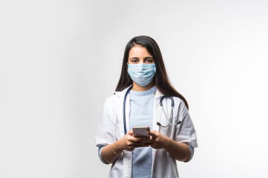Hintli kadın doktor akıllı telefondan konuşuyor. Heyecanlı, koronavirüs salgınında tıbbi maske takıyor.