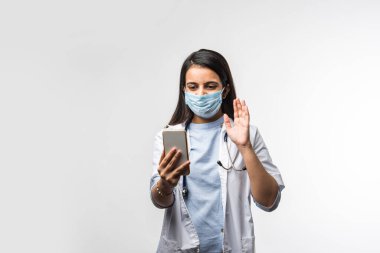 Hintli kadın doktor akıllı telefondan konuşuyor. Heyecanlı, koronavirüs salgınında tıbbi maske takıyor.