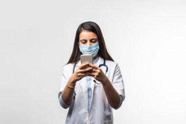 Hintli kadın doktor akıllı telefondan konuşuyor. Heyecanlı, koronavirüs salgınında tıbbi maske takıyor.