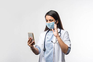 Hintli kadın doktor akıllı telefondan konuşuyor. Heyecanlı, koronavirüs salgınında tıbbi maske takıyor.