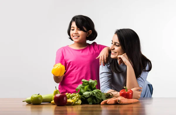 Beautiful Indian / Asian young Mother and Daughter posing or playing at table full of fruits and vegetables