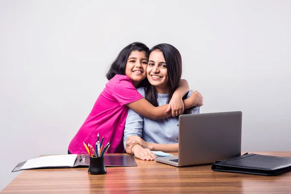 Working Indian mom works from home office with kid in pandemic. Woman and cute child using laptop. Freelancer workplace in cozy home. Happy mother and daughter.