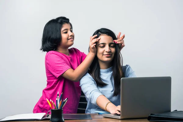 Working Indian mom works from home office with kid in pandemic. Woman and cute child using laptop. Freelancer workplace in cozy home. Happy mother and daughter.