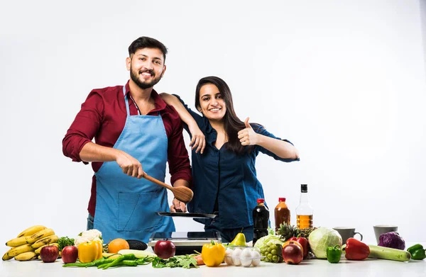 Indian couple in kitchen - Young Beautiful asian wife enjoying cooking with husband with lots of fresh vegetables and fruits