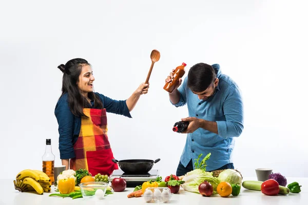Indian couple in kitchen - Young Beautiful asian wife enjoying cooking with husband with lots of fresh vegetables and fruits