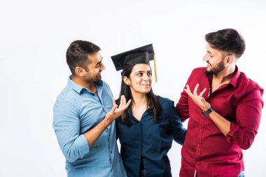 Güzel genç Hintli kız öğrenci mezuniyet töreninde erkek arkadaşıyla başarıyı kutlarken beyaz arka planda şapka takıyor.