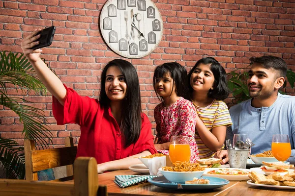 Indian young Family of four eating food at dining table at home or in restaurant. South Asian mother, father and two daughters having meal together