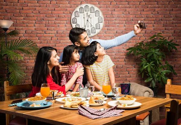 Indian young Family of four eating food at dining table at home or in restaurant. South Asian mother, father and two daughters having meal together