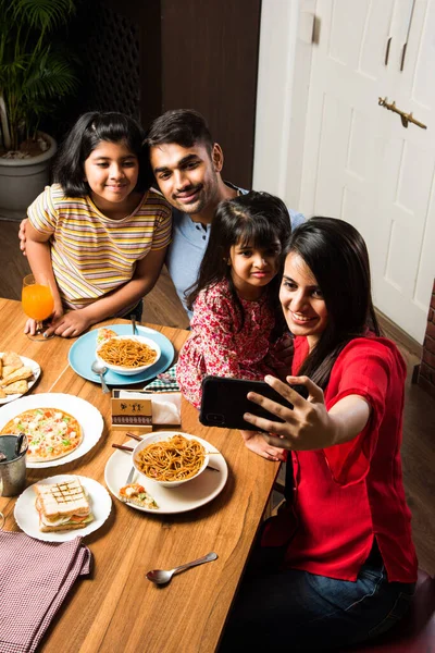 Indian young Family of four eating food at dining table at home or in restaurant. South Asian mother, father and two daughters having meal together