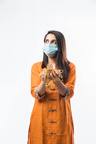 Indian woman holding gold jewelry, ornaments while wearing medical face mask in corona or covid-19 Pandemic- Asset or Gold Loan concept