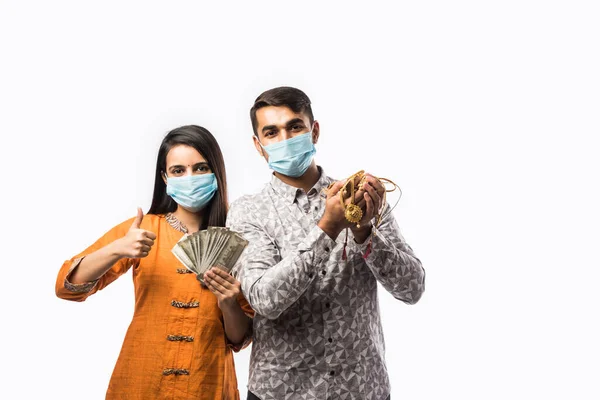 Indian couple holding gold jewelry, ornaments while wearing medical face mask in corona or covid-19 Pandemic- Asset or Gold Loan concept