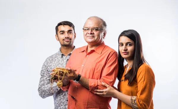 Indian old man with young son and daughter or couple holding gold jewelry, ornaments - Asset or Gold Loan concept