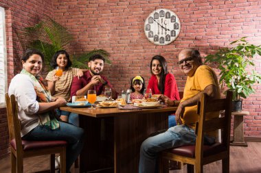 Hindistan 'ın çok nesilli ailesi yemek masasında yemek yiyor. Güney Asyalı büyükbaba, anne, baba ve iki kız birlikte yemek yiyorlar.
