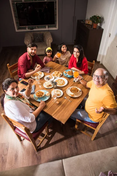 Indian multigenerational Family eating food at dining table at home or restaurant. South Asian grandfather, mother, father and two daughters having meal together