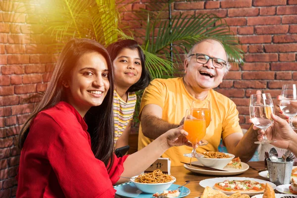 Indian multigenerational Family eating food at dining table at home or restaurant. South Asian grandfather, mother, father and two daughters having meal together