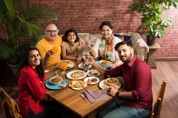 Indian multigenerational Family eating food at dining table at home or restaurant. South Asian grandfather, mother, father and two daughters having meal together